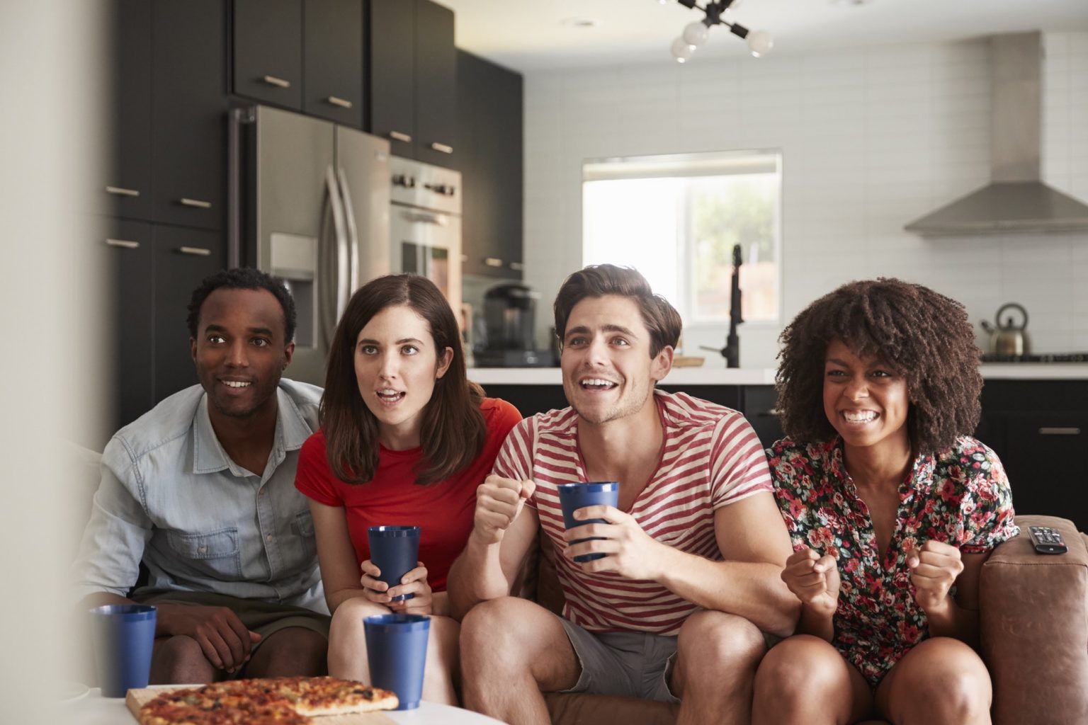 Four young adult friends watching sports on TV at home