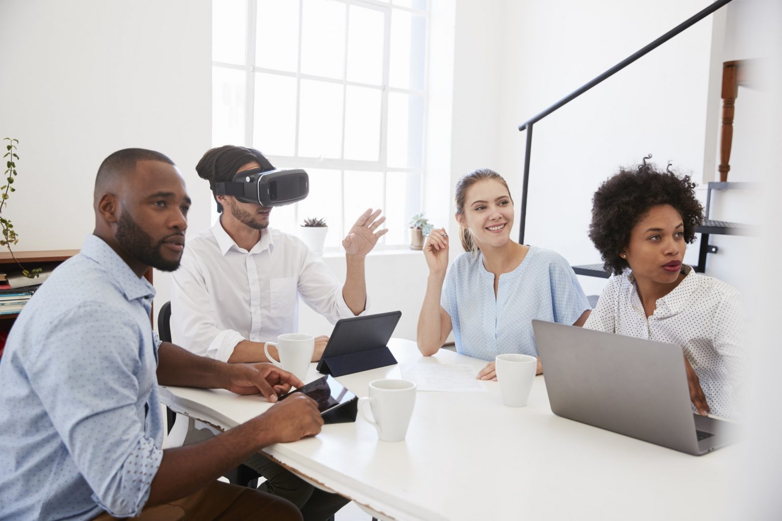 Man in VR goggles at a desk with colleagues in an office