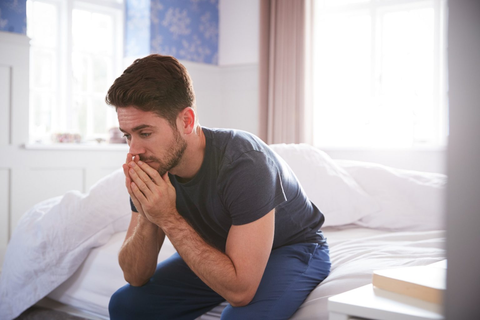 Man Wearing Pajamas Suffering With Depression Sitting On Bed At Home