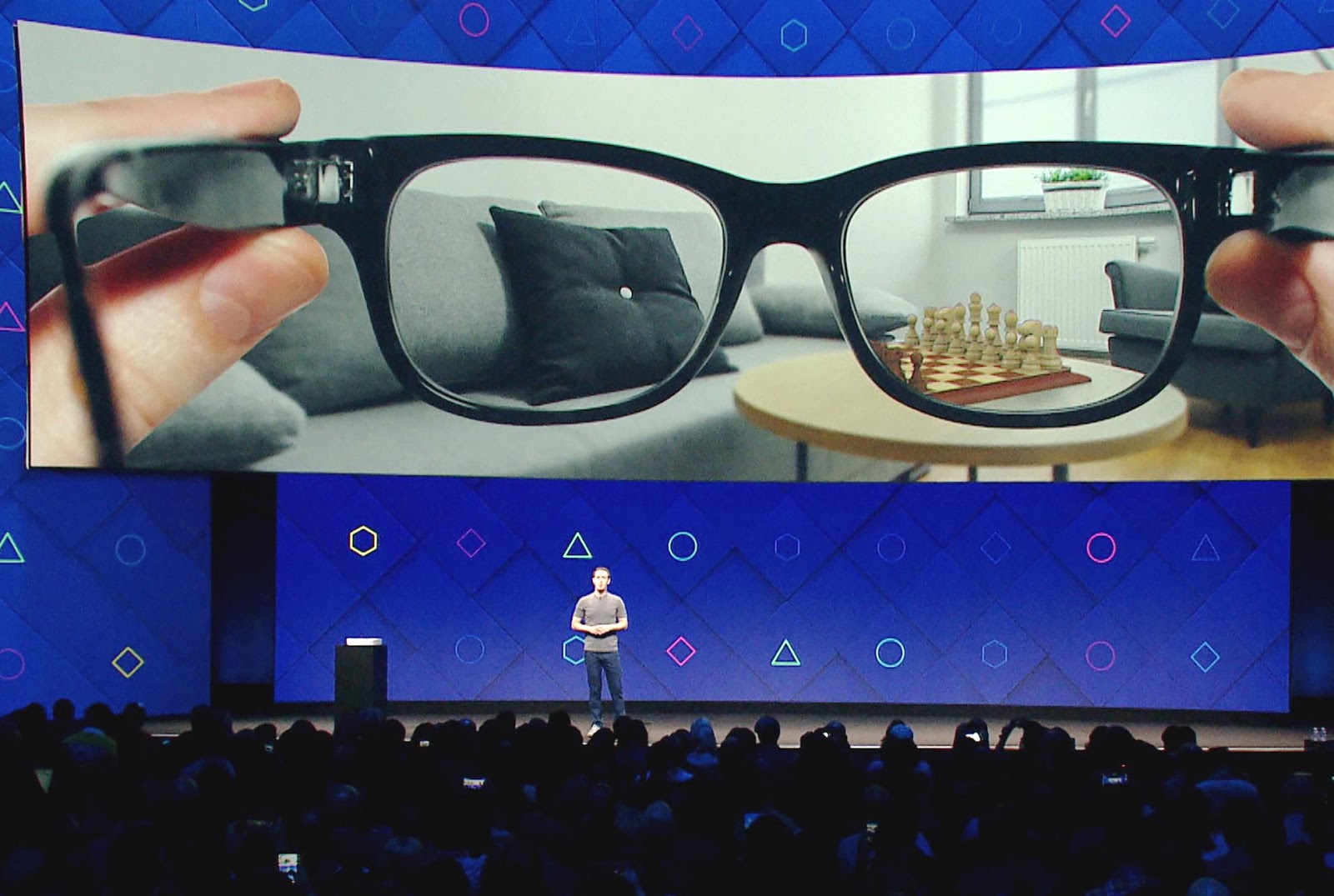 Mark Zuckerberg on stage in front of an image of smart glasses